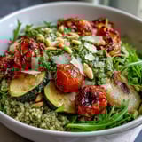 A warm serving of Arugula Pesto Bowl with quinoa and roasted veggies, drizzled generously with vibrant homemade pesto.