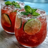 Two vibrant glasses of Guava Juice With Sparkling Water topped with mint leaves and set on a sunny patio table.