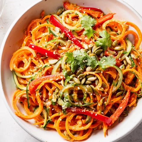 The Carrot Noodle Skincare Bowl features a zesty tahini-lime drizzle over fresh spinach and red peppers, served in a bright, healthy lunch bowl.