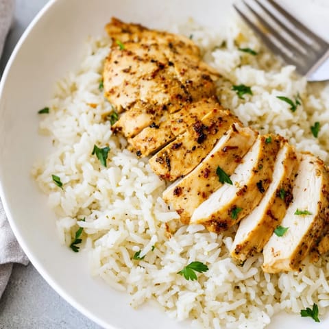 Fluffy garlic butter rice with tender grilled chicken pieces, served hot in a white bowl with fresh herbs for a comforting meal.