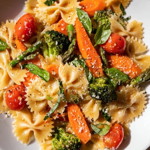 A steaming skillet of Rainbow Veggie Pasta Primavera features red peppers, broccoli, and peas, garnished with fresh basil and a lemon wedge.