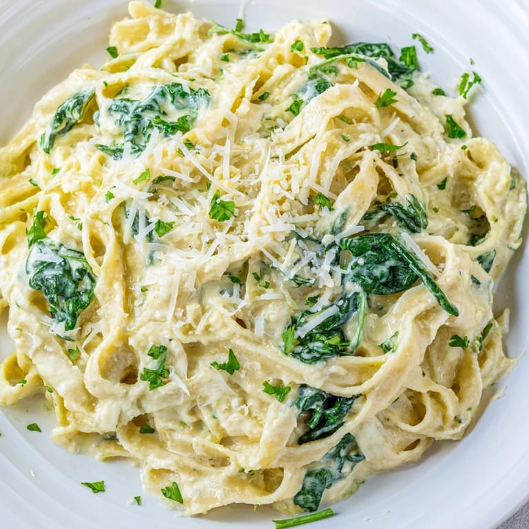Tender fettuccine coated in creamy spinach Alfredo, topped with Parmesan; a delicious vegetarian meal.