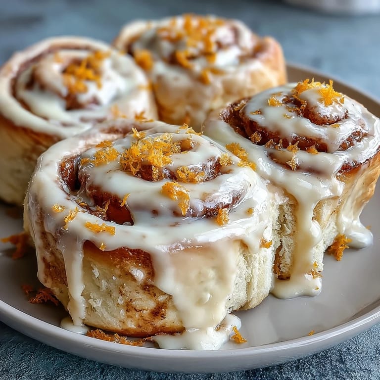 Warm orange rolls topped with luscious cream cheese frosting, their citrus aroma and soft texture inviting a cozy breakfast or brunch treat.